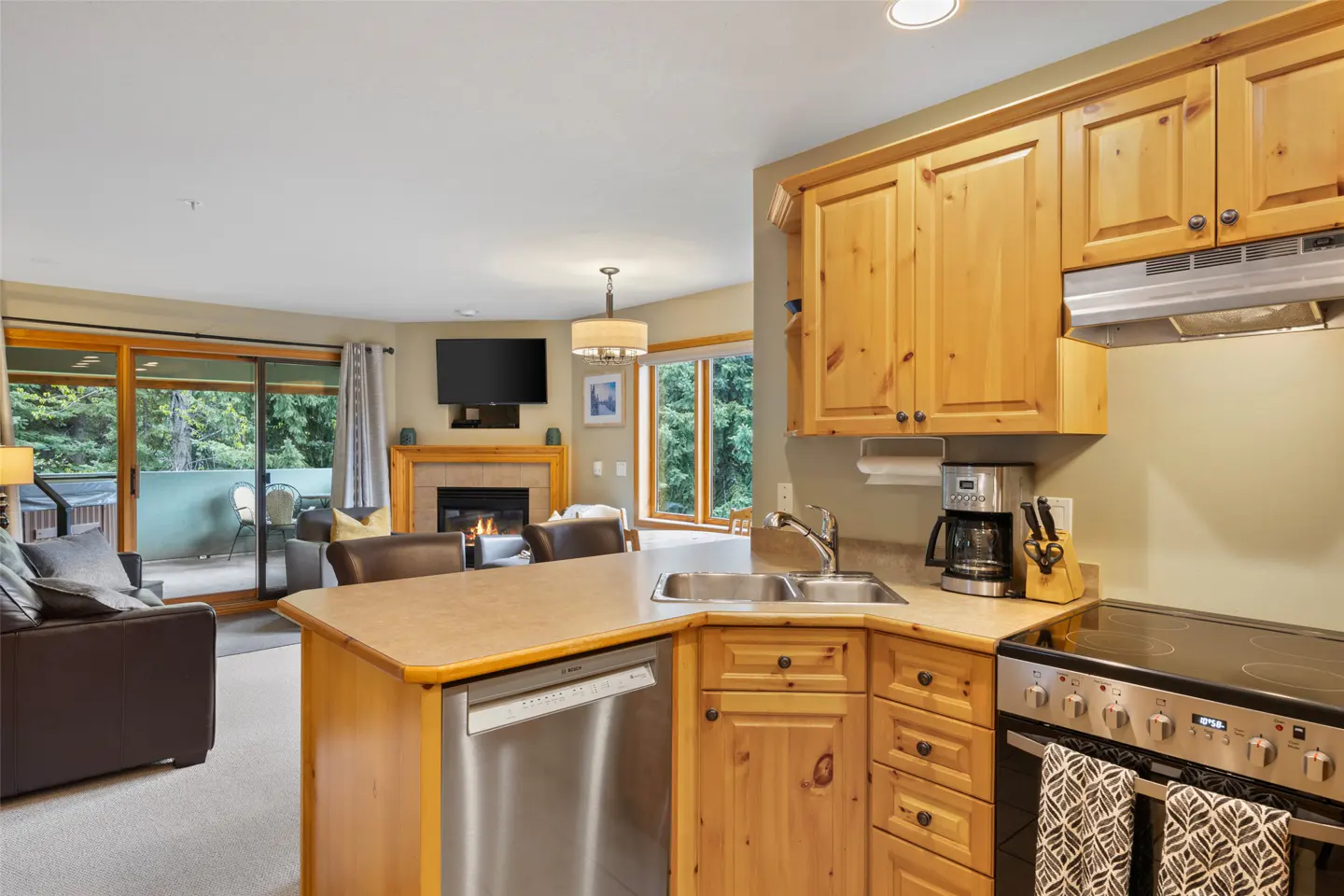 Open concept living space with wood cabinets, stainless steel appliances, and a fireplace. A brown leather couch is visible.