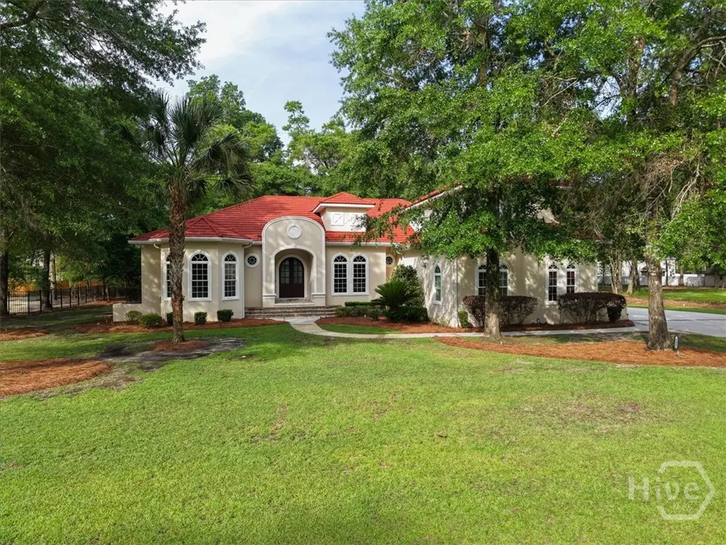 Beige house with a red tile roof, arched windows, and a green lawn surrounded by trees.