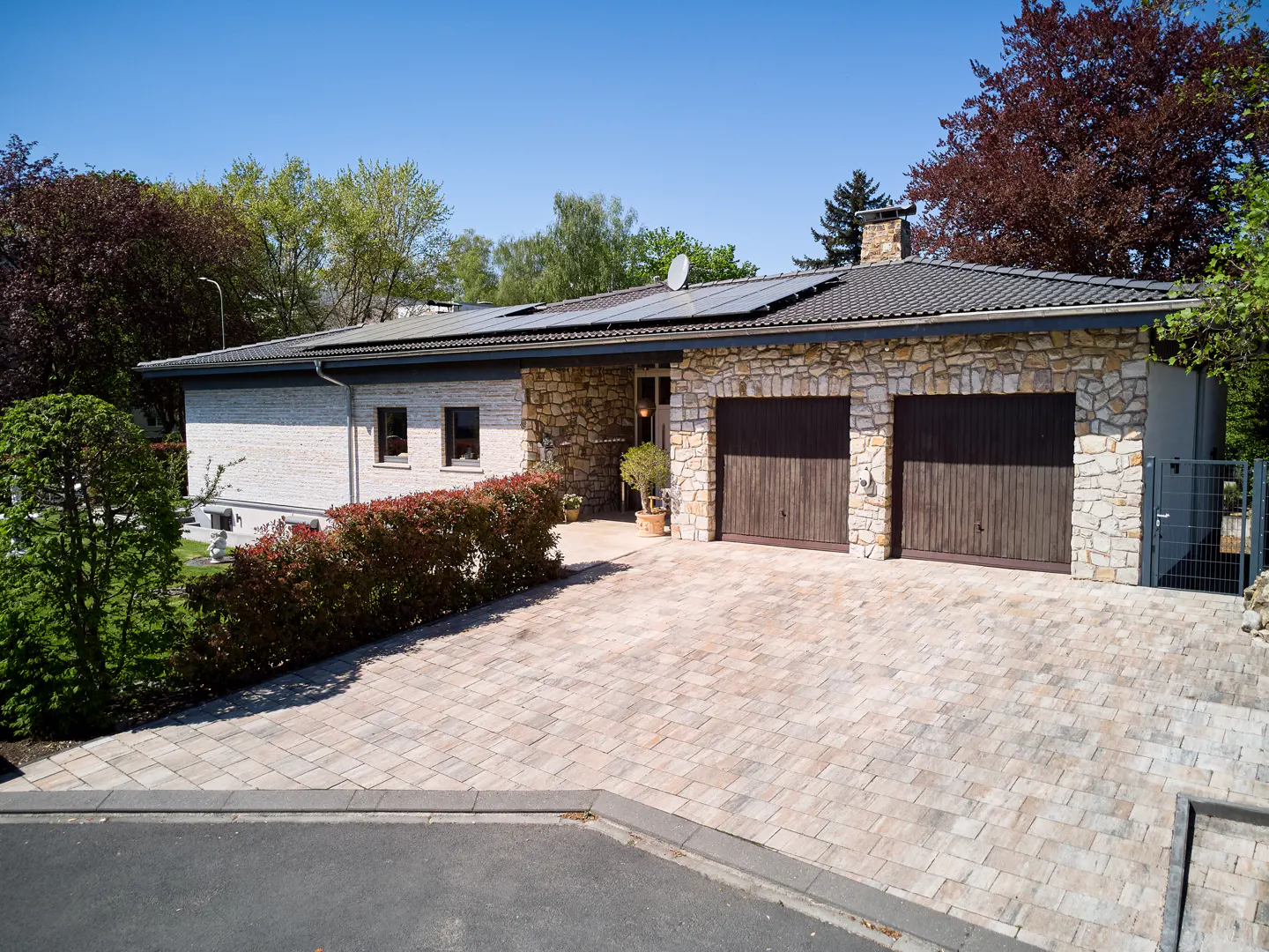 A single-story house with a stone facade, a two-car garage, and a paved driveway on a sunny day.