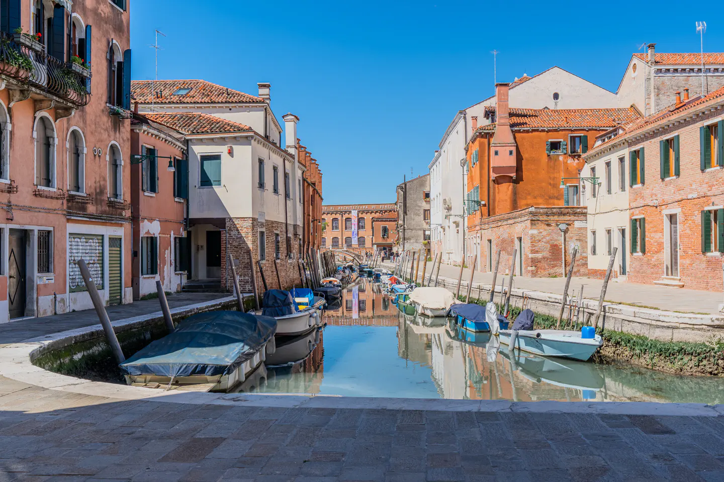 Venice canal view with boats docked along colorful buildings under a clear blue sky.