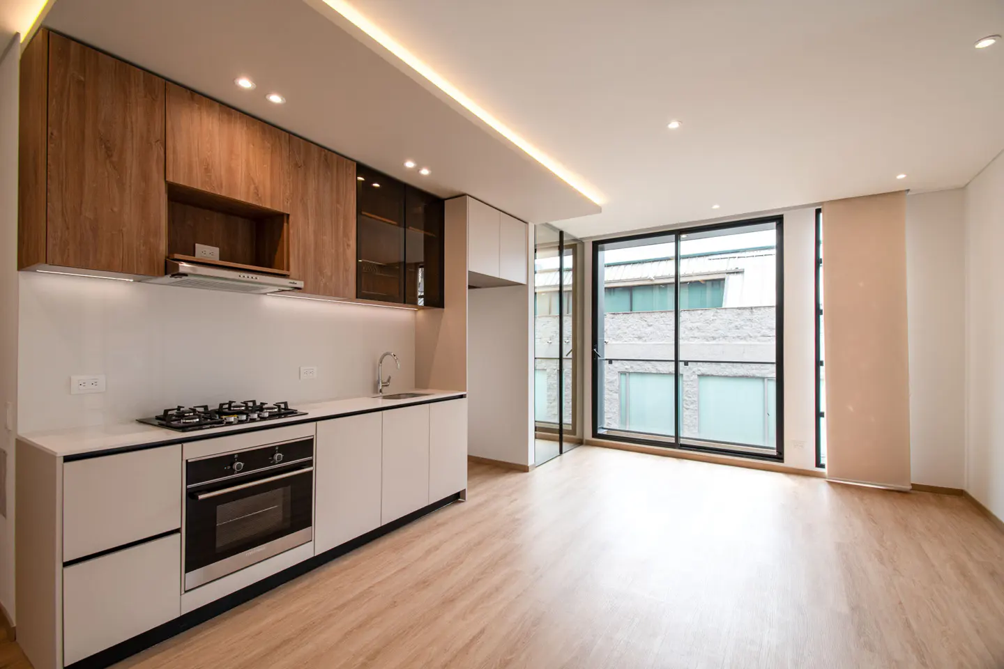 A modern kitchen with wood cabinets, white countertops, and stainless steel appliances, next to a large window.