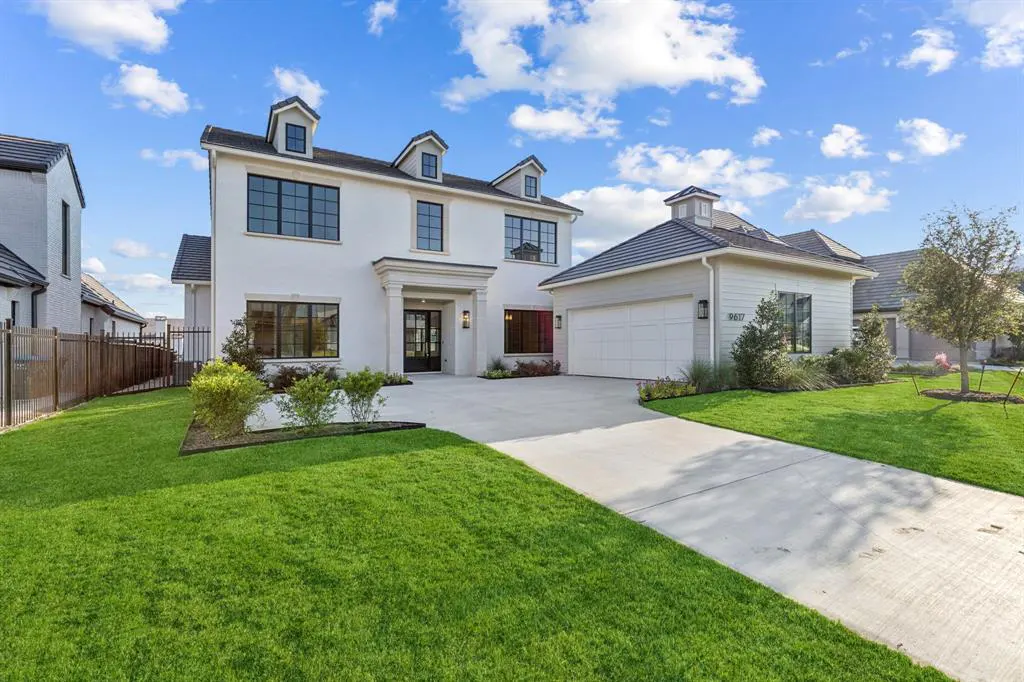 Two-story white house with black trim, dormers, and a two-car garage on a green lawn under a blue sky.