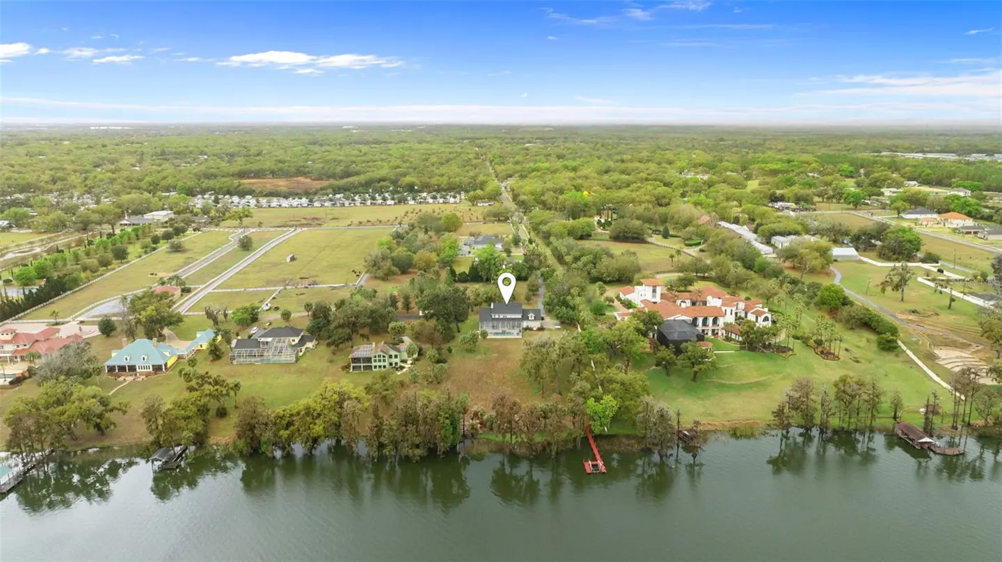 Aerial view of a lakefront property with a gray house, red dock, and lush green trees under a blue sky.