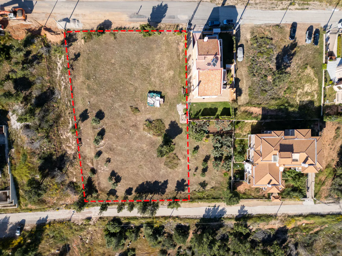Aerial view of a vacant lot outlined in red, with sparse vegetation, near houses and a road.