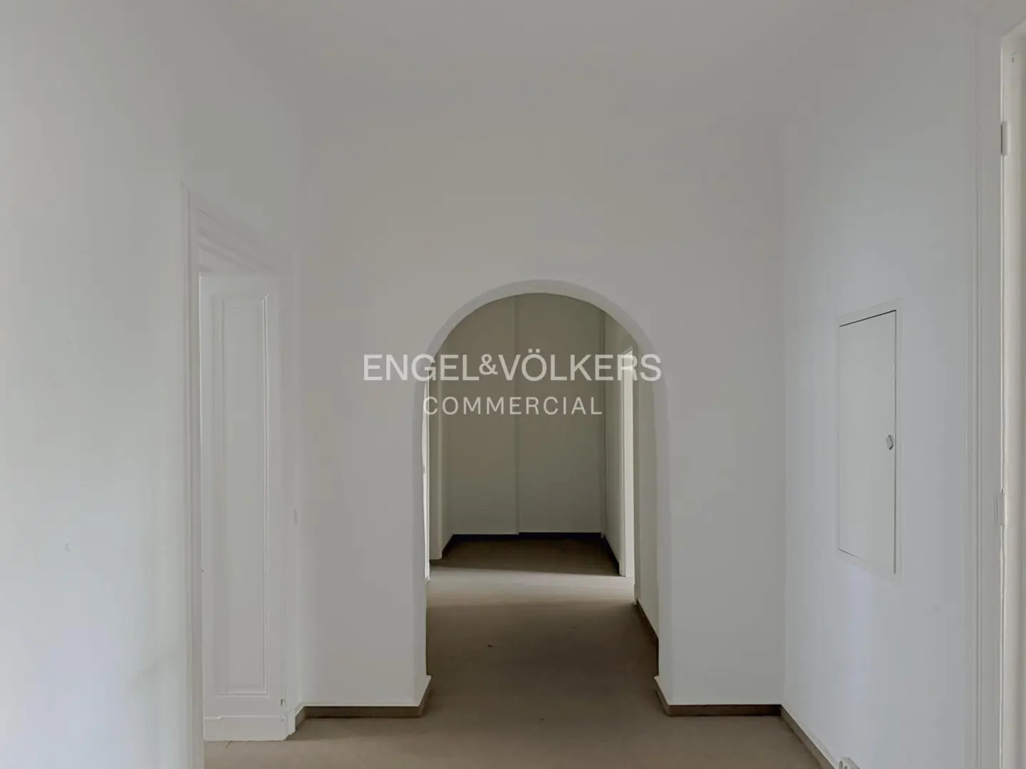 Interior view of a white-walled commercial space with an arched doorway and the Engel & Völkers logo.