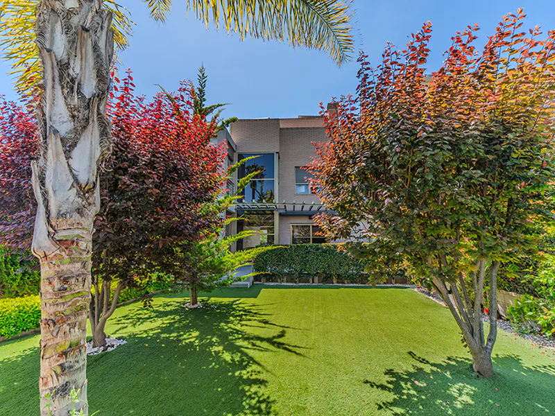 Modern two-story house with brick facade, green lawn, and trees with red leaves under a clear blue sky.