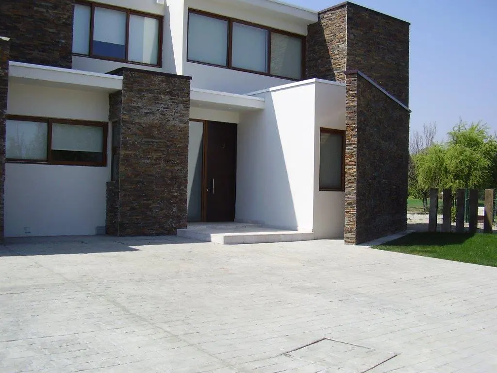 Modern two-story house with white walls, brown trim, and stone accents. A paved driveway leads to the front door.