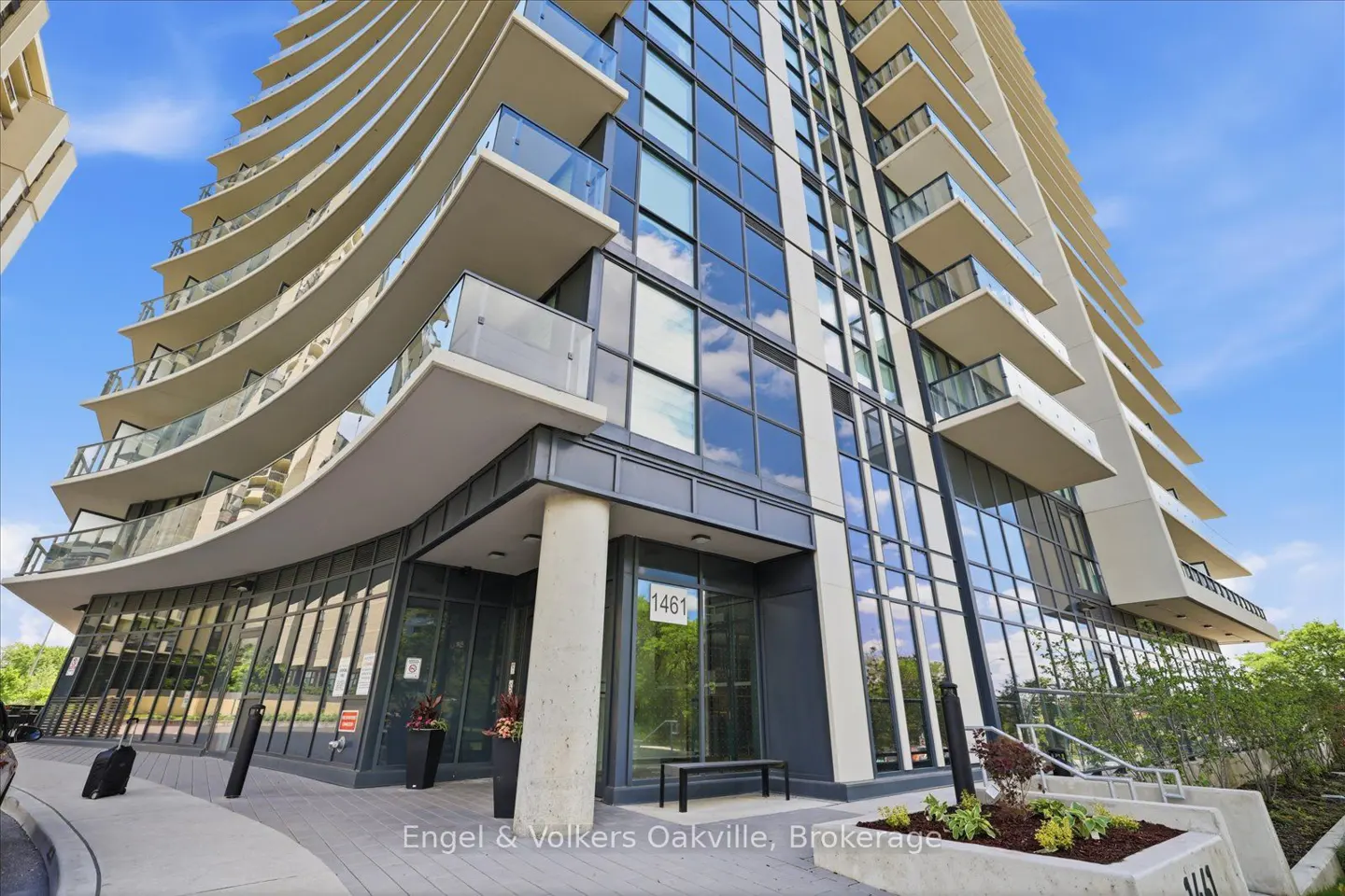 Low-angle view of a modern high-rise apartment building with curved balconies and glass windows under a blue sky.