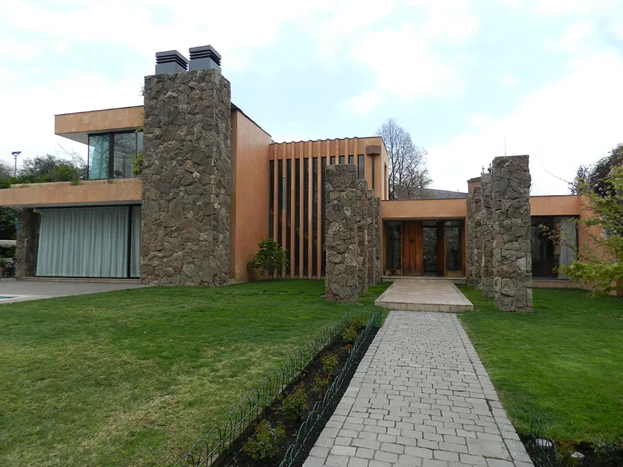 Modern two-story house with stone pillars and chimneys, peach-colored walls, and a stone walkway leading to the front door.