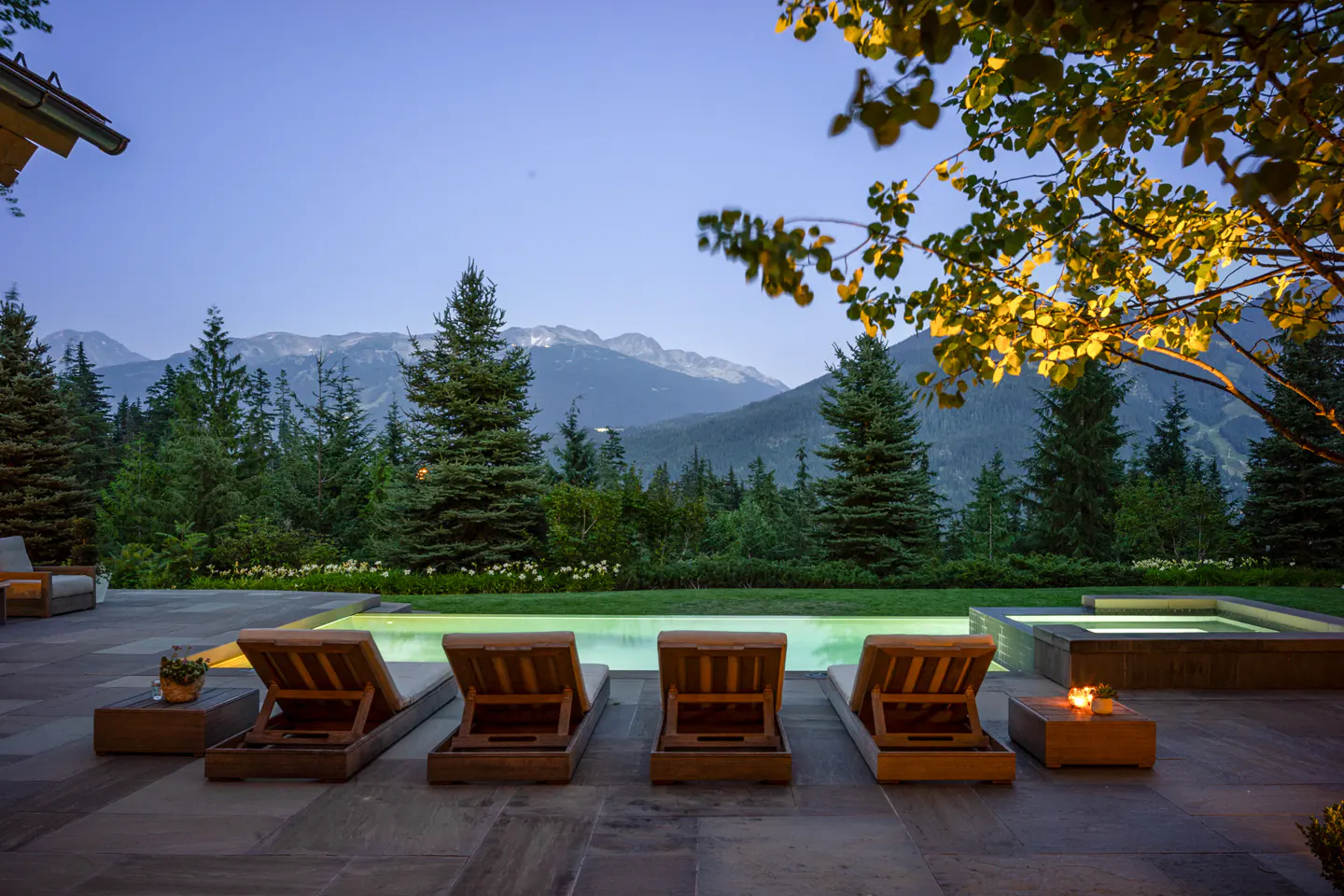 Outdoor pool area with four lounge chairs facing a mountain view.