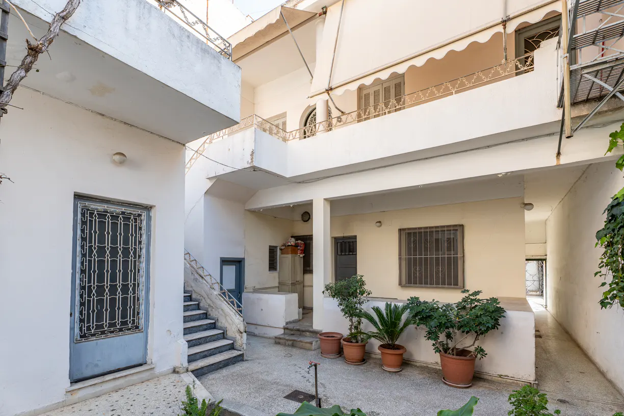 Exterior view of a multi-story white building with a courtyard, potted plants, and stairs.