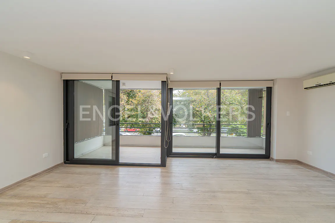 Bright, empty room with beige tile floor and large sliding glass doors to a balcony with trees visible.