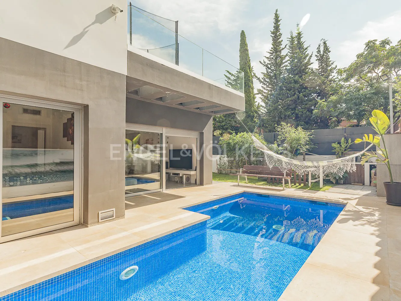 Modern home exterior with a blue tiled pool, a hammock, and sliding glass doors leading to the interior.