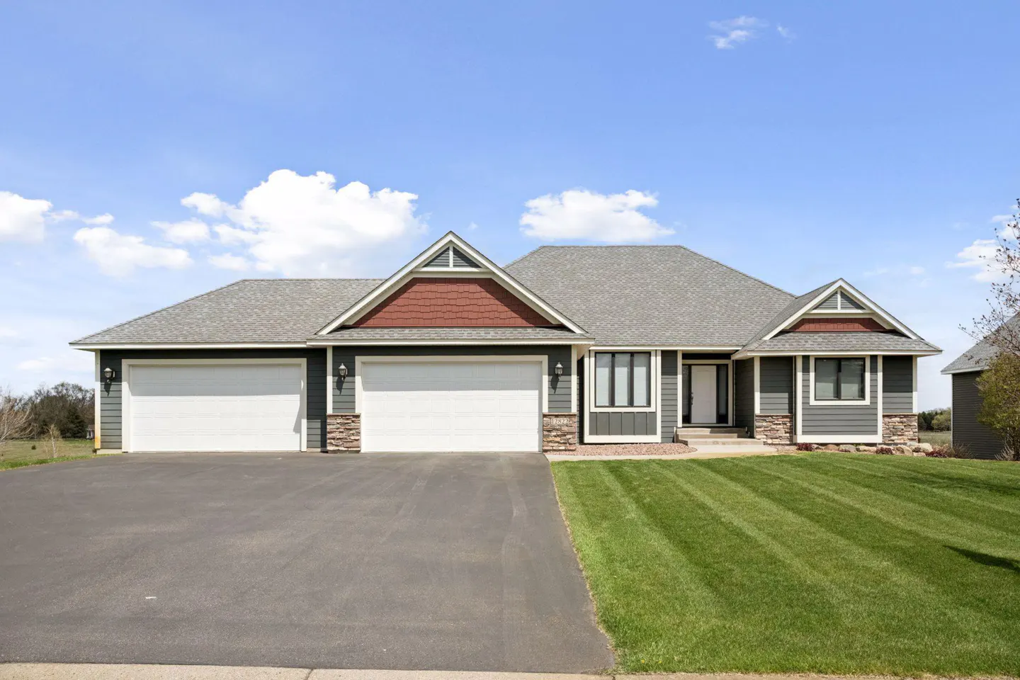 A single-story house with a gray exterior, white garage doors, and a well-manicured lawn.
