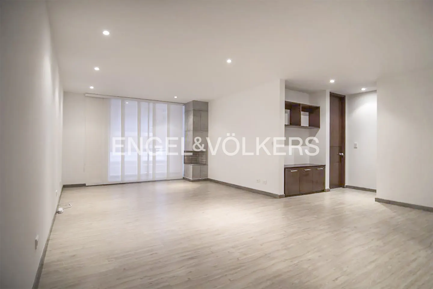 Spacious, minimalist living room with light wood floors, white walls, a corner fireplace, and dark wood built-in cabinets.