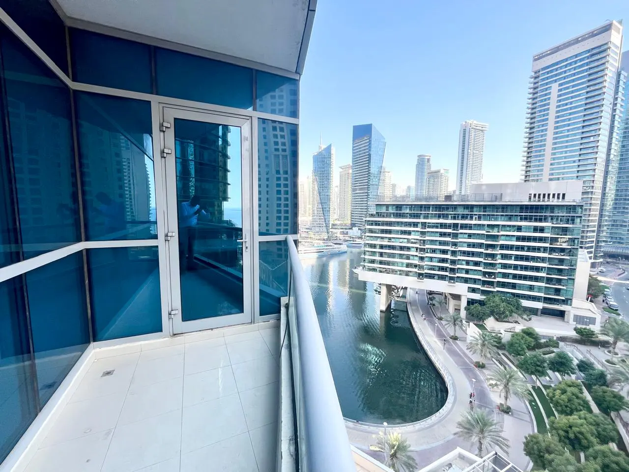 Balcony view of Dubai Marina with blue glass windows, skyscrapers, and a waterway.
