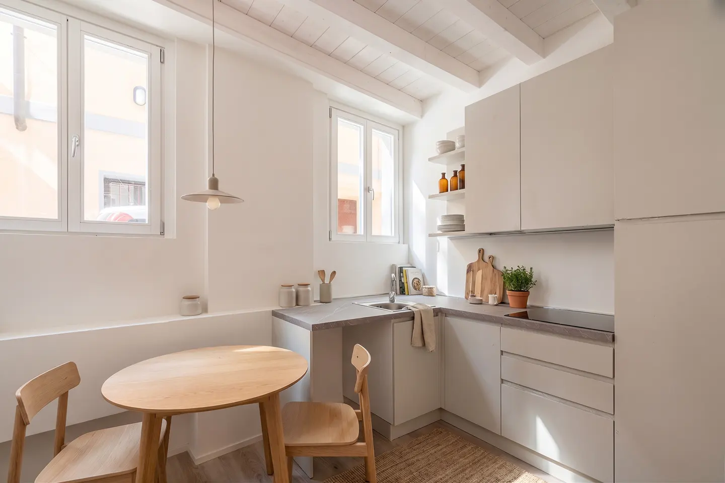 Bright, modern kitchen with white cabinets, wooden dining table, two chairs, and natural light from two windows.
