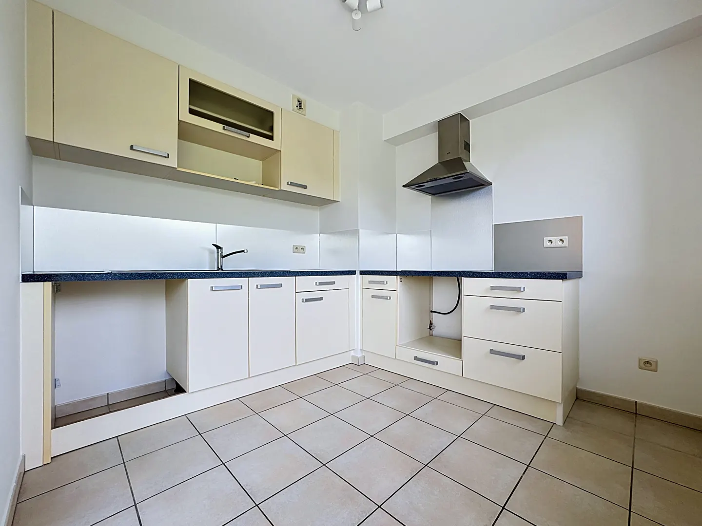 A bright kitchen with cream cabinets, a dark countertop, and a stainless steel range hood. The floor is tiled in a neutral color.