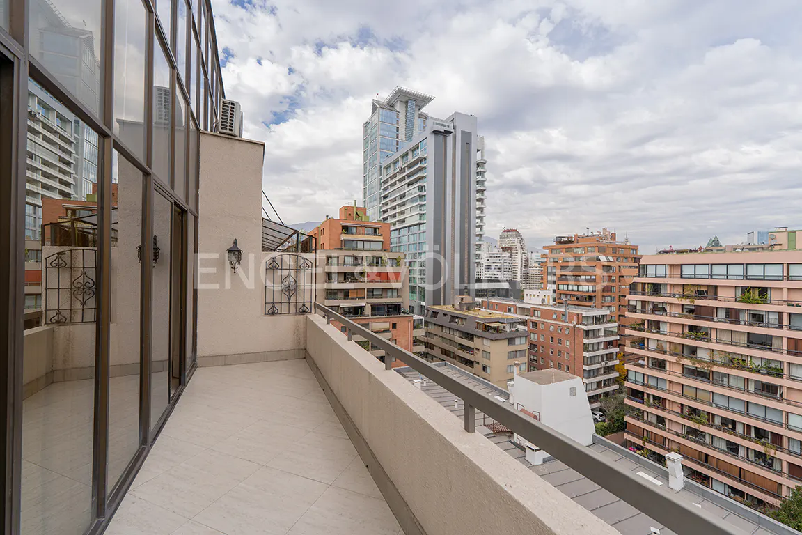 Balcony view of a city skyline. The balcony has a tile floor and metal railing. Tall buildings are in the background under a cloudy sky.