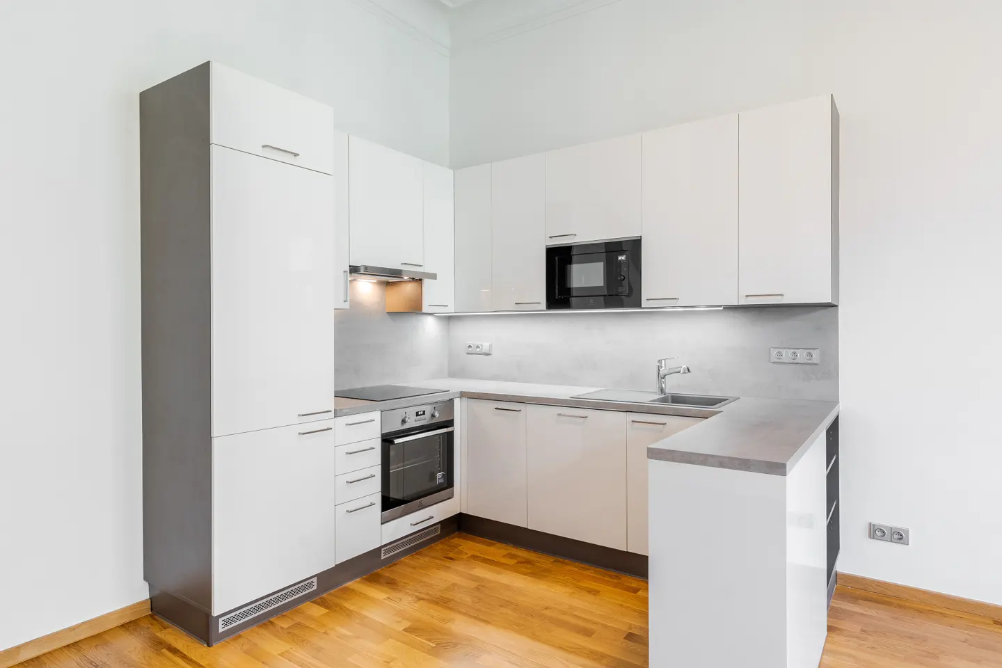 Bright kitchen with white cabinets, gray countertops, and wood floors. Oven, microwave, and sink are visible.