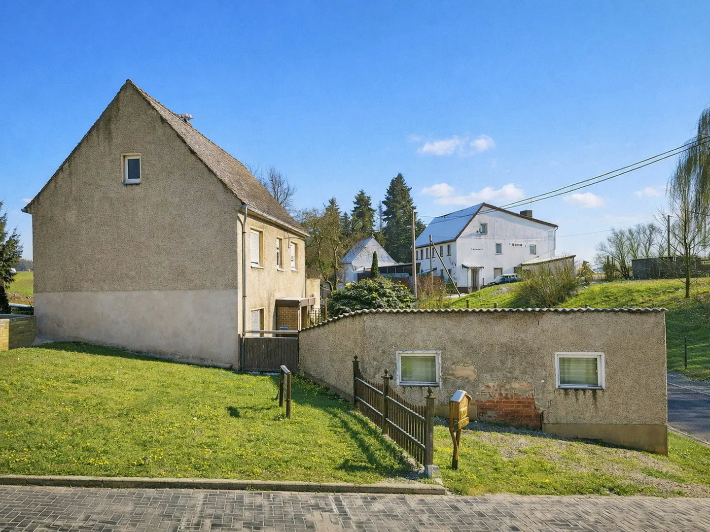Exterior view of a two-story stucco house with a gabled roof, a low wall, and a green lawn under a clear blue sky.