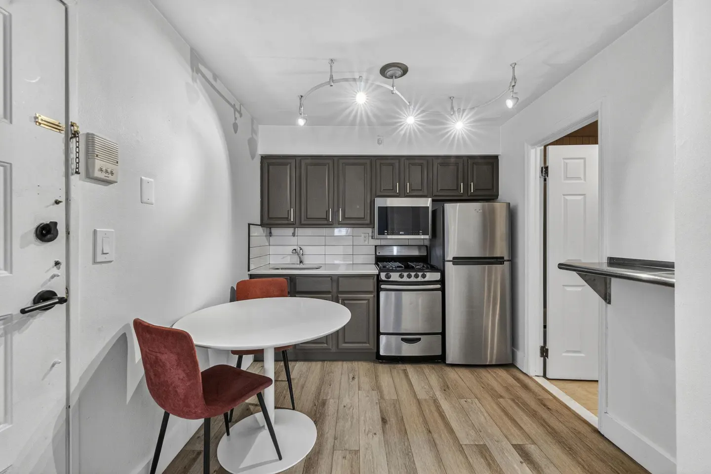 Small kitchen with dark cabinets, stainless steel appliances, white subway tile backsplash, and a round white dining table.
