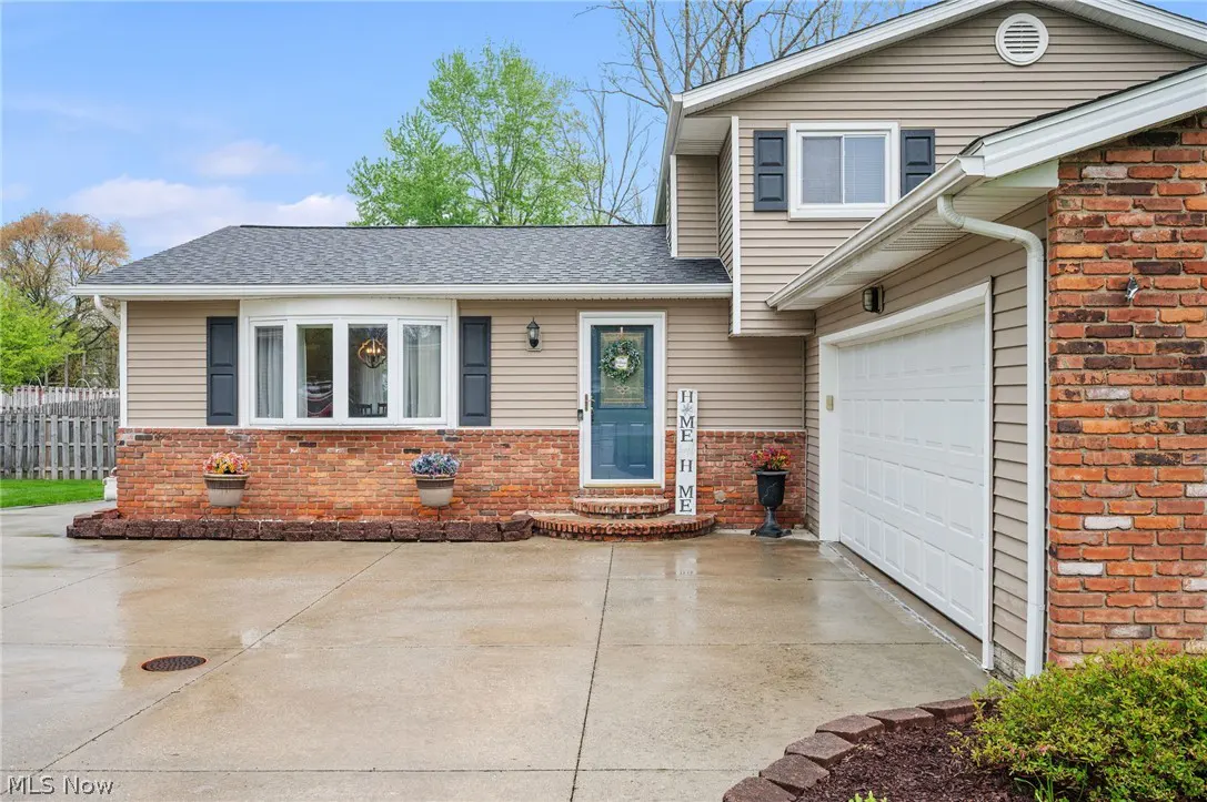 Two-story house with tan siding, brick accents, a blue front door with a wreath, and a white garage door.