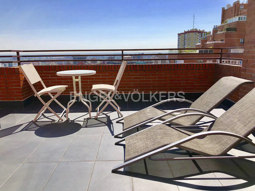 Rooftop patio with two lounge chairs, a small table, and two folding chairs, with a brick wall and city view.