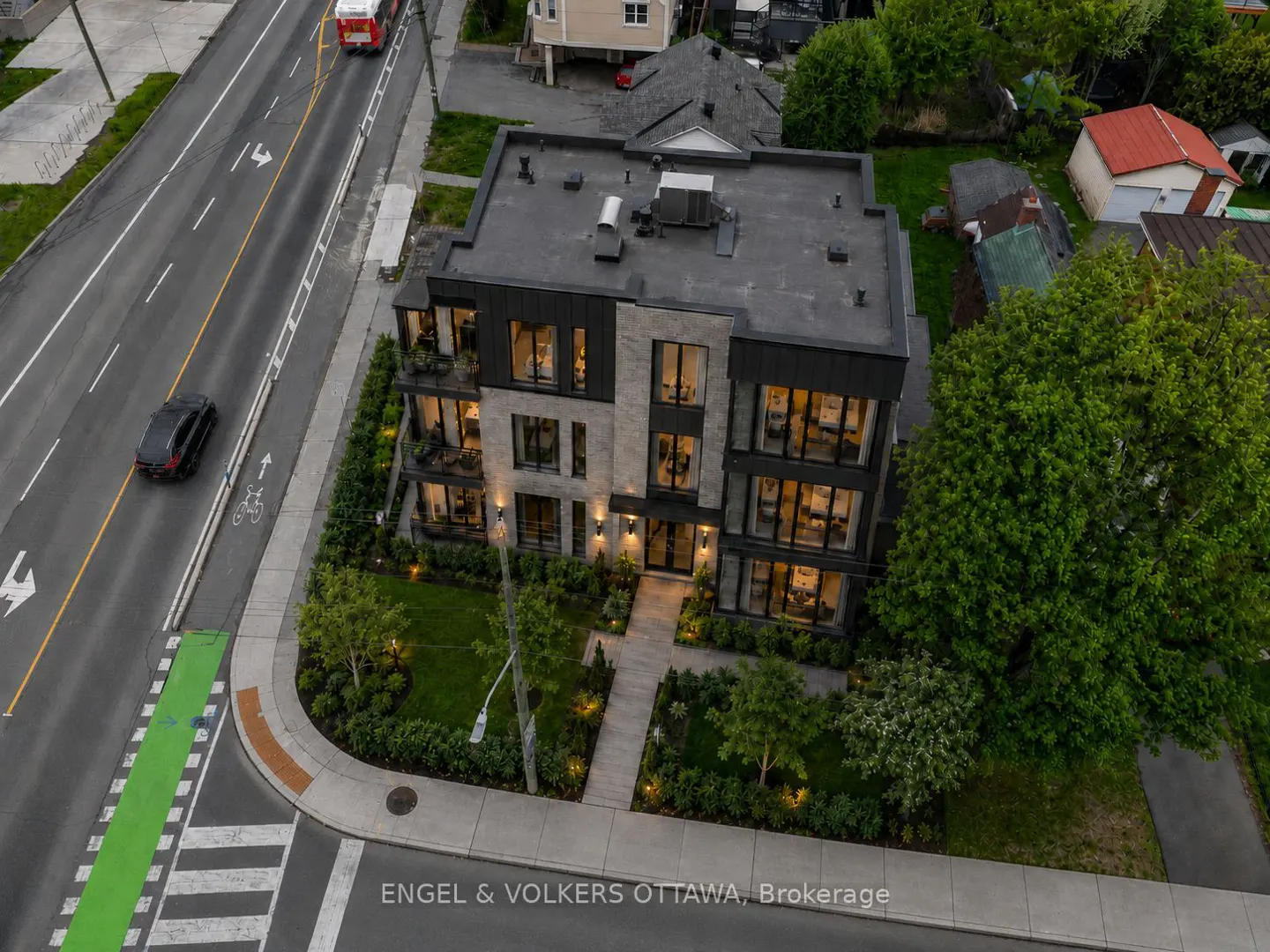 Aerial view of a modern, multi-story grey brick apartment building with black trim, located on a corner lot near a road.