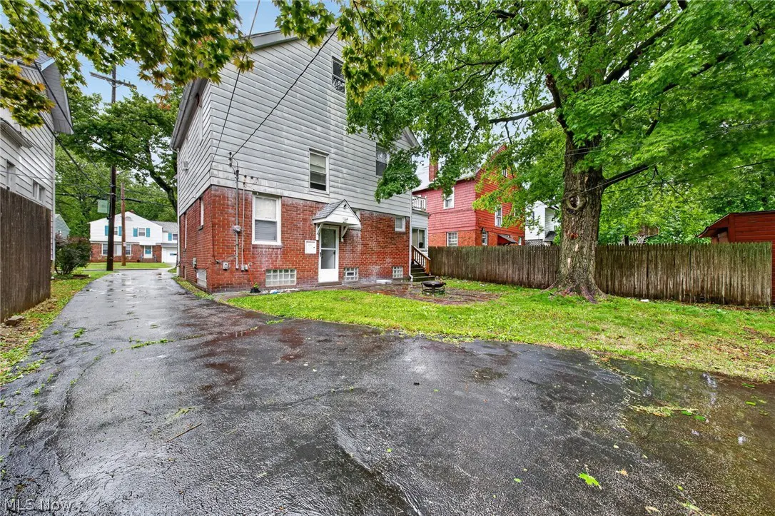 Backyard view of a two-story house with gray siding and a brick foundation, a wet driveway, and a wooden fence.