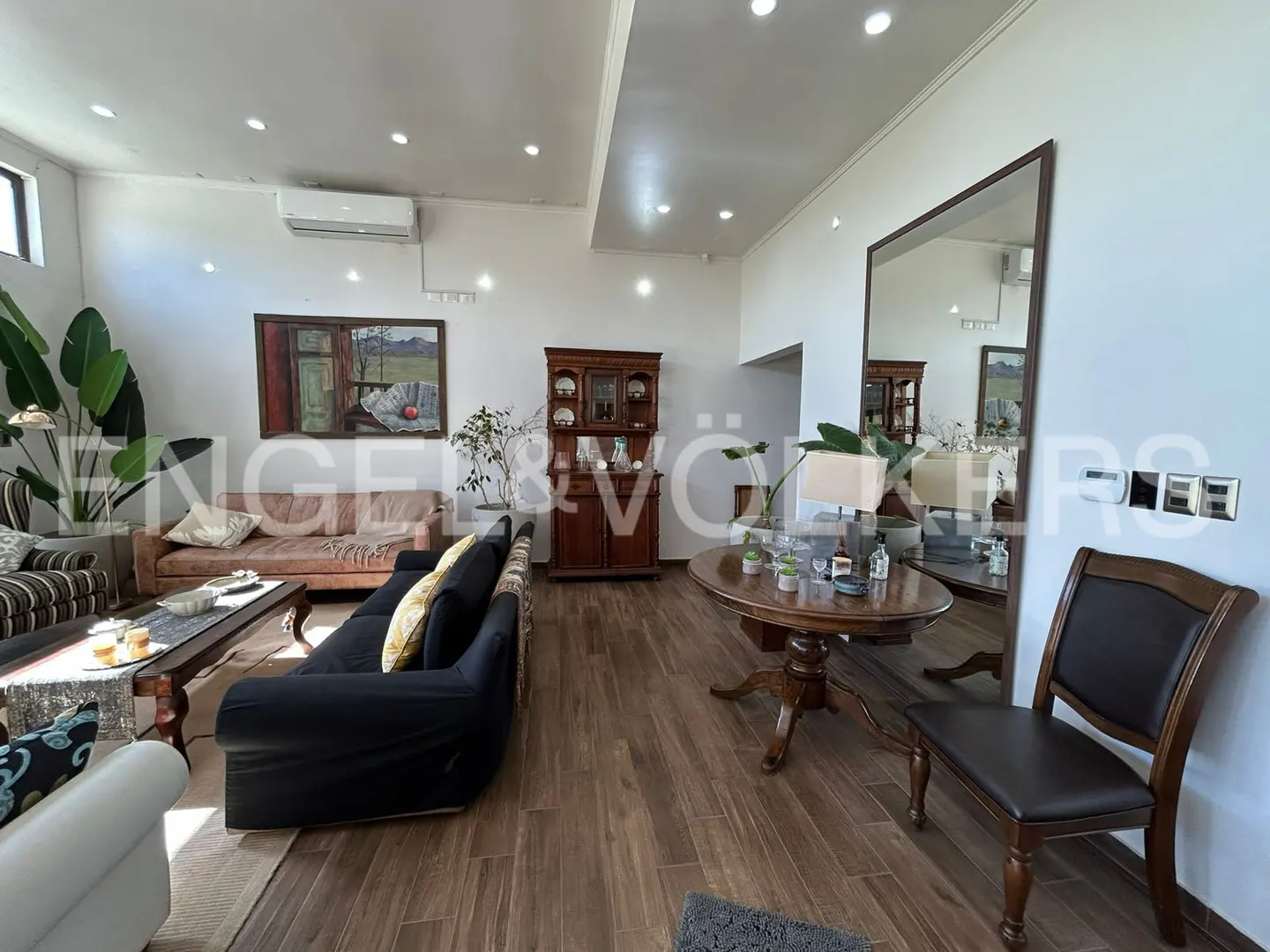 A living room with hardwood floors, sofas, a wooden table, a mirror, and a painting.