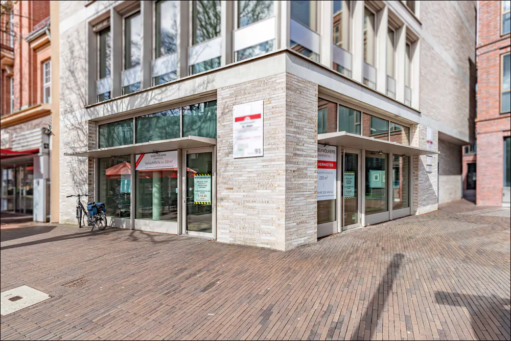 Exterior view of a commercial building with glass windows and doors, brick facade, and brick-paved sidewalk. A bicycle is parked nearby.