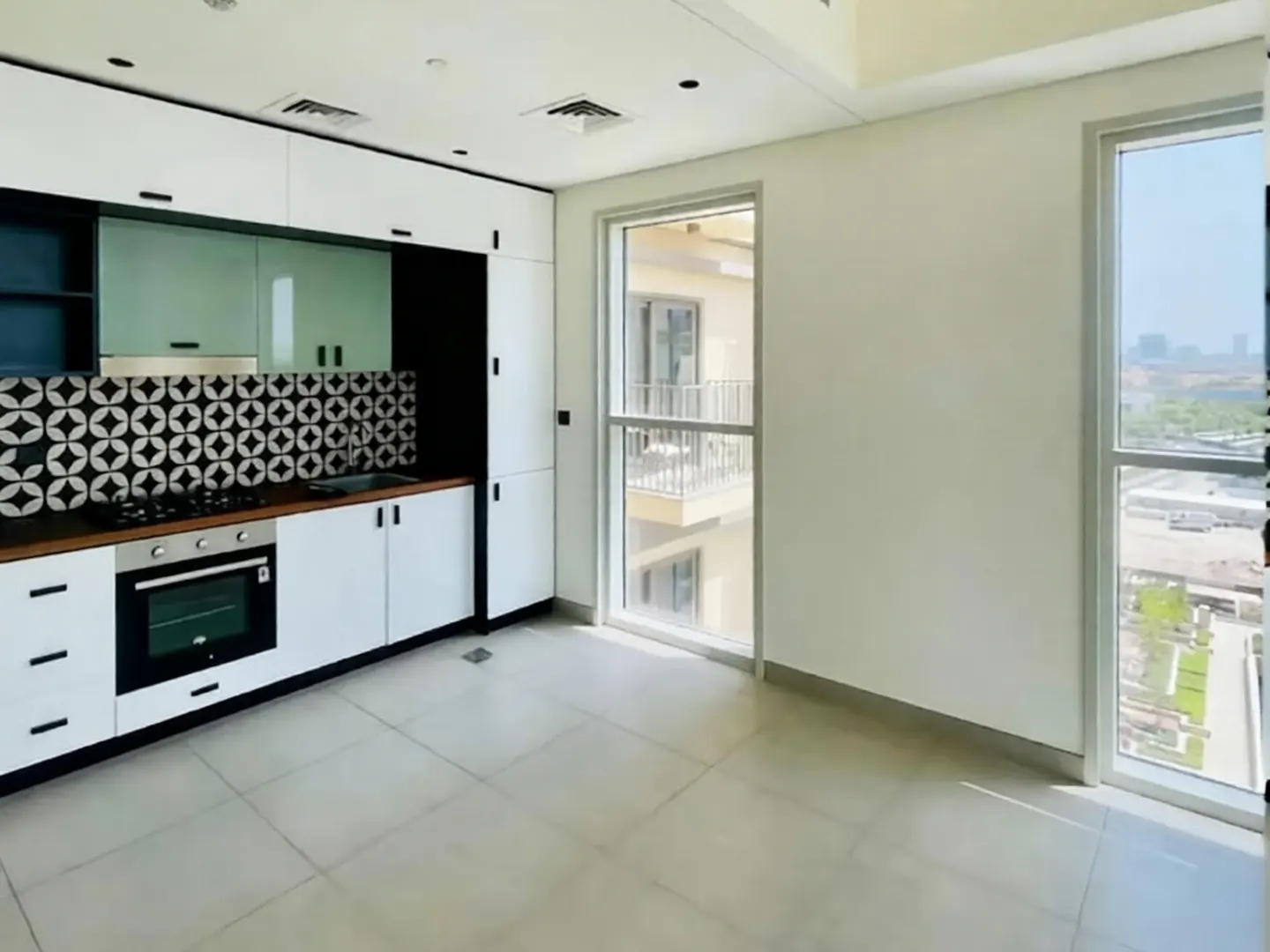 Bright kitchen with white cabinets, black hardware, and geometric backsplash. Large windows offer a city view.