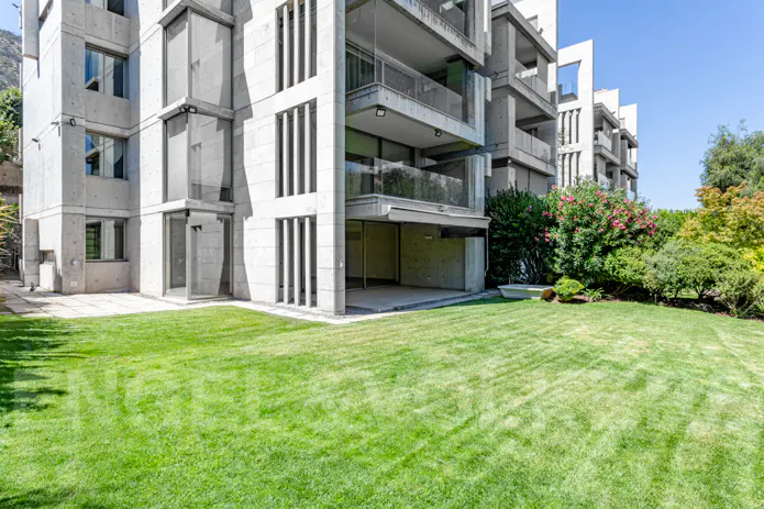 Modern concrete apartment building with balconies and a green lawn. Trees and shrubs are visible in the background.