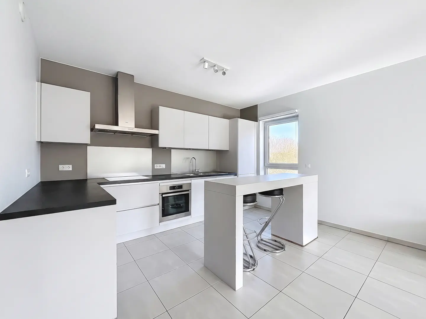 Bright, modern kitchen with white cabinets, black countertops, stainless steel appliances, and a white island with two chrome bar stools.