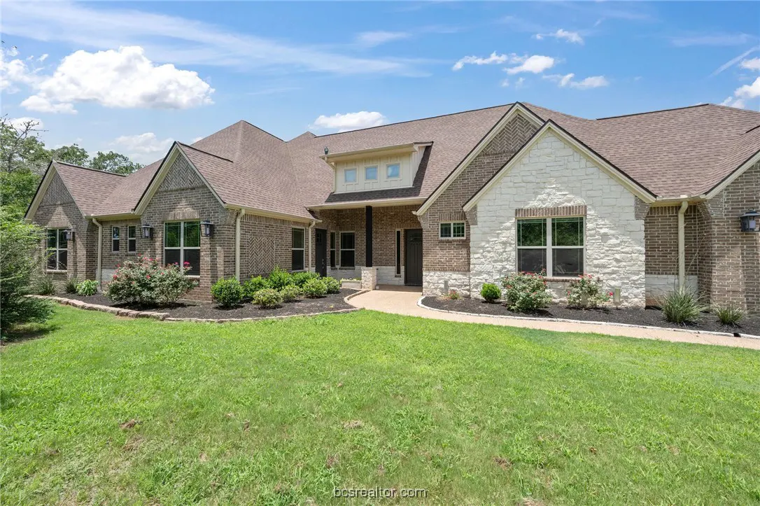 A single-story brick house with a brown roof, white stone accents, and a green lawn under a blue sky.