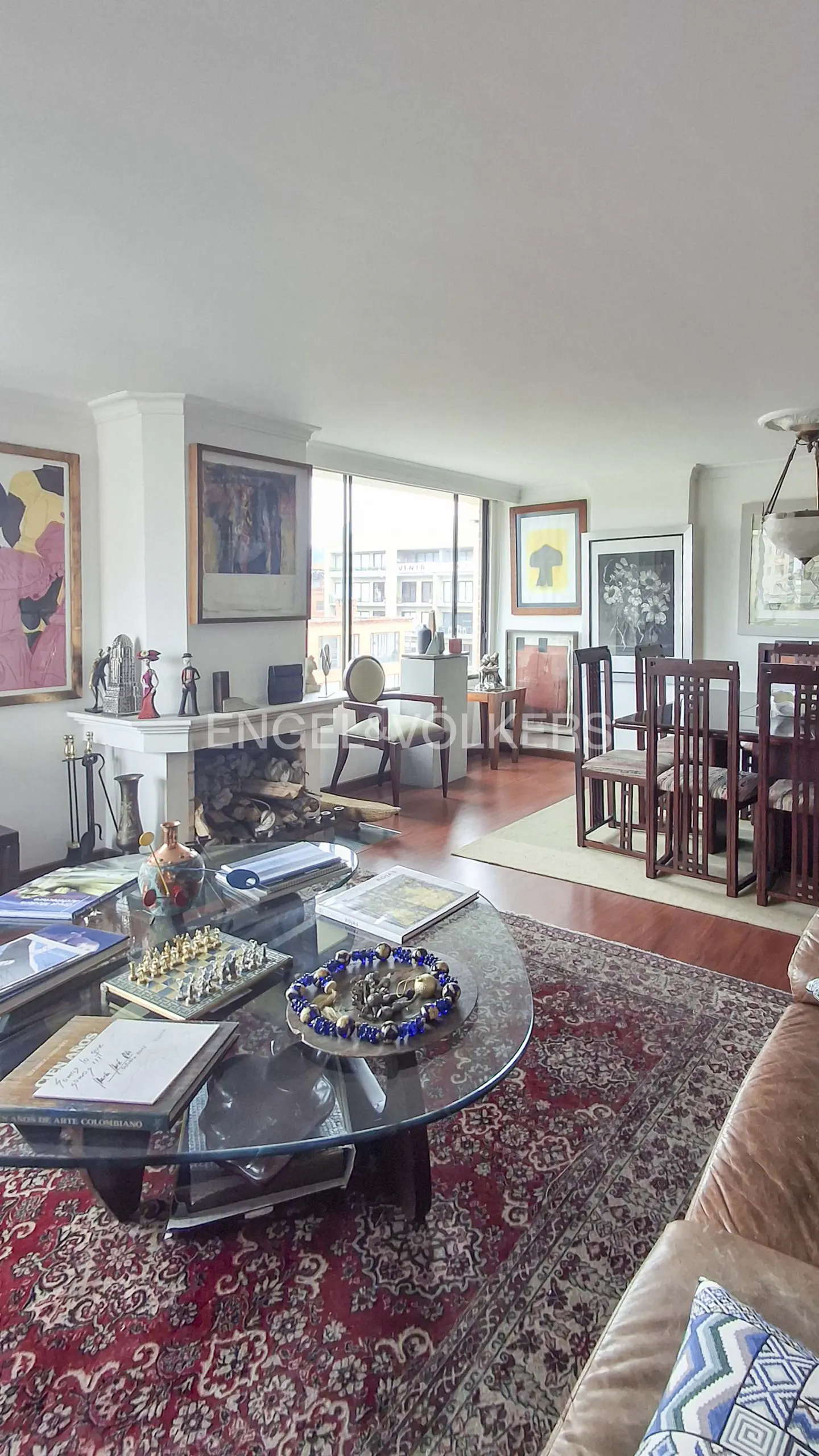 Wide shot of a living room with a glass coffee table, fireplace, art, and dining set.