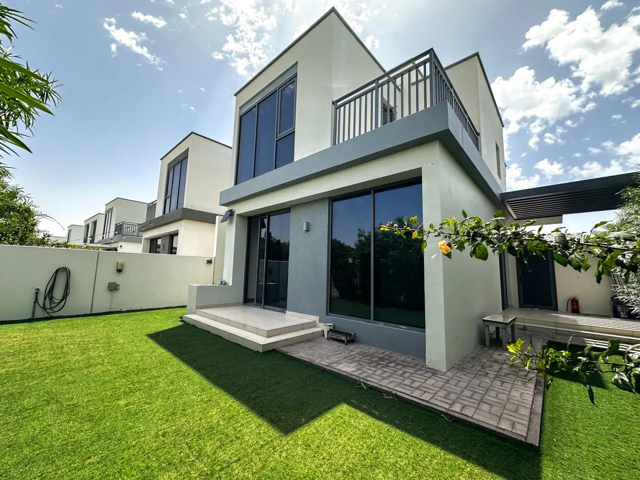Two-story modern house with a balcony, large windows, and a green lawn under a blue sky.