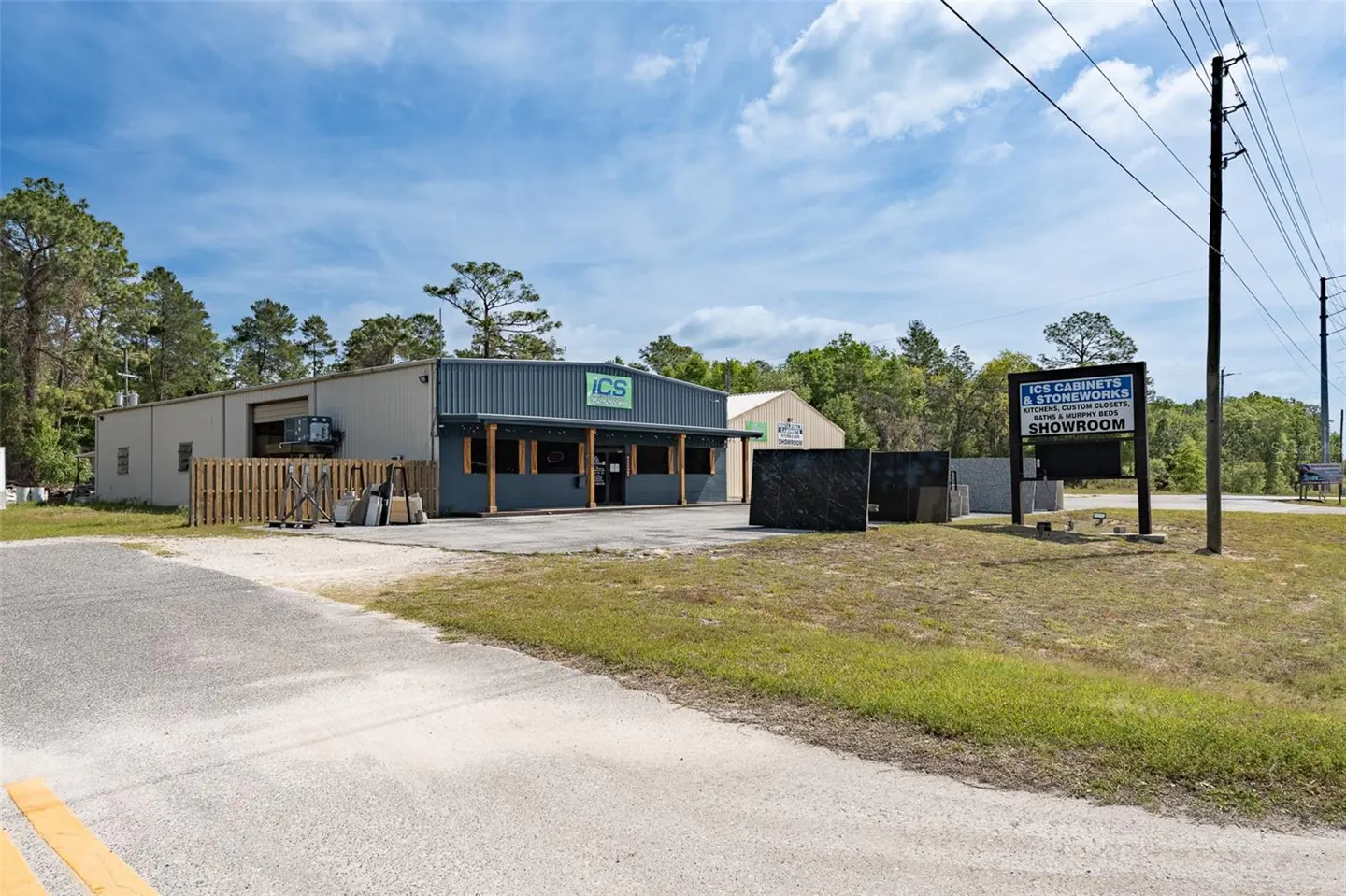 Exterior view of ICS Cabinets & Stoneworks showroom, a gray building with a green logo, under a blue sky.
