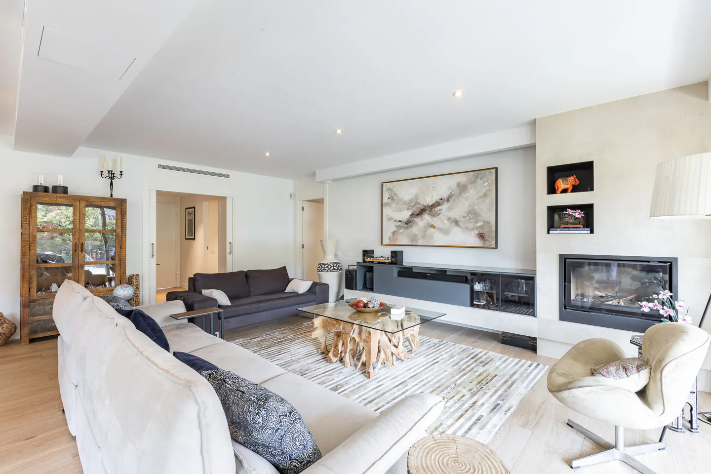 Bright living room with white walls, light wood floors, and modern furniture. A large abstract painting hangs above a fireplace.