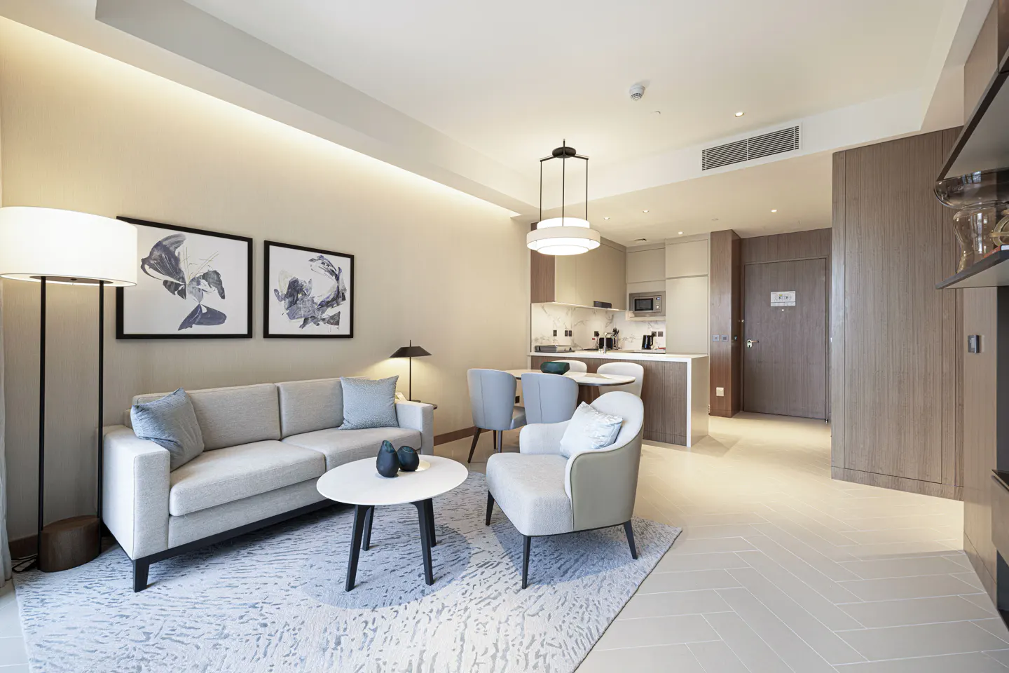 A modern apartment living room with a sofa, chair, table, and open kitchen. Neutral colors and contemporary design.