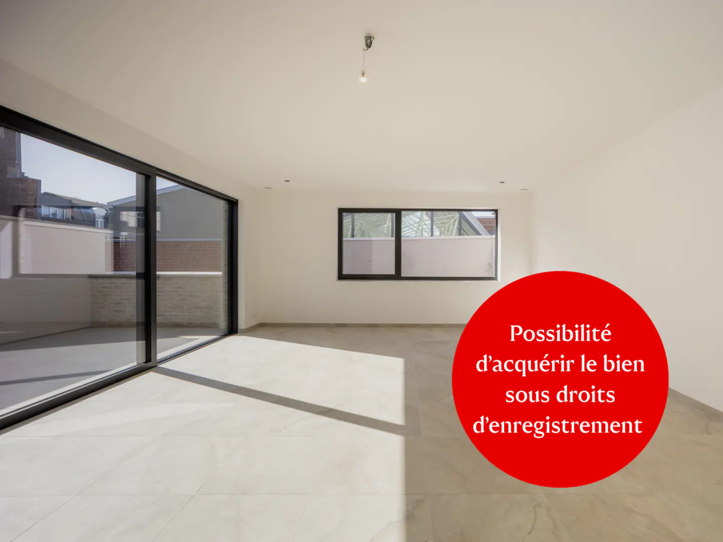 Bright, empty room with white walls, light gray tile floor, and large black-framed windows. A red circle with white text is superimposed on the image.