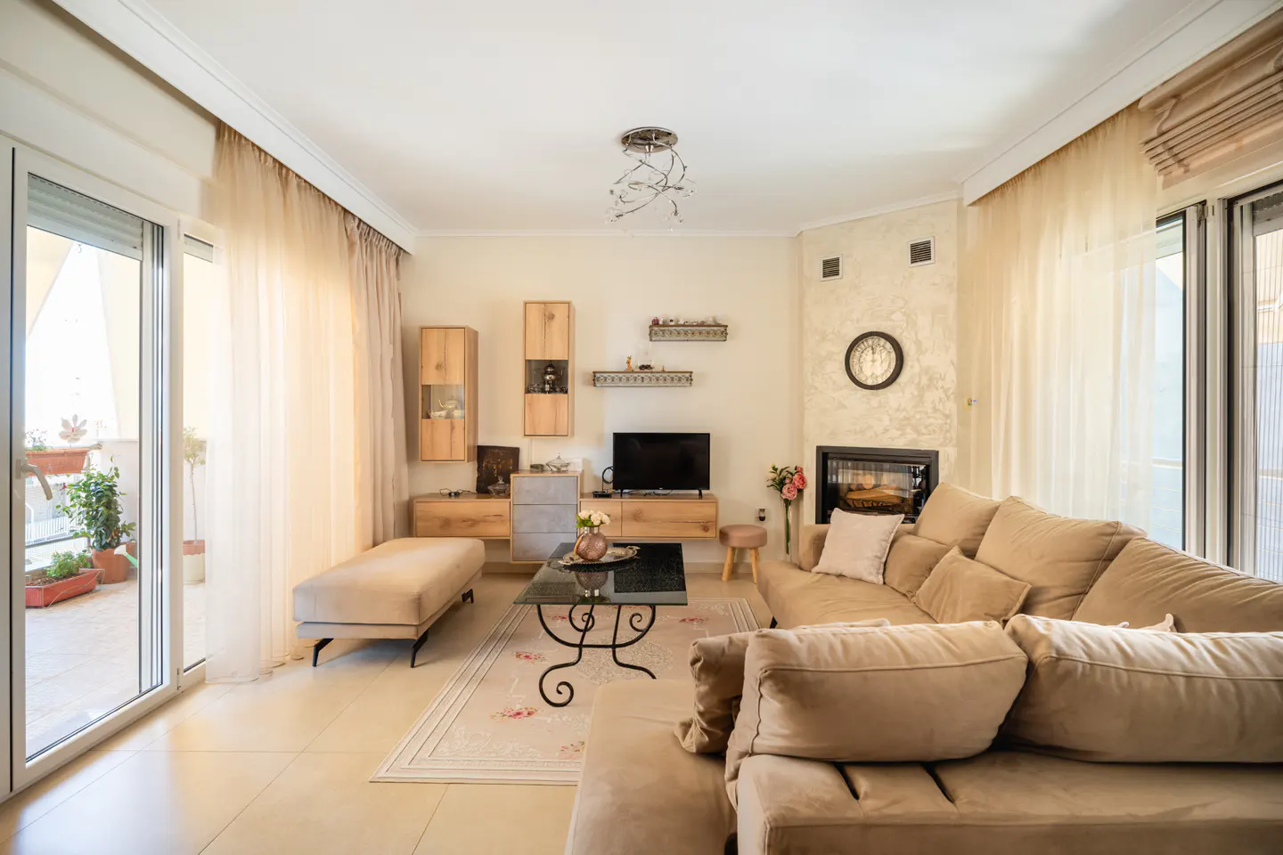 A bright living room with a beige sectional sofa, glass coffee table, and a fireplace. Sliding glass doors lead to a balcony.