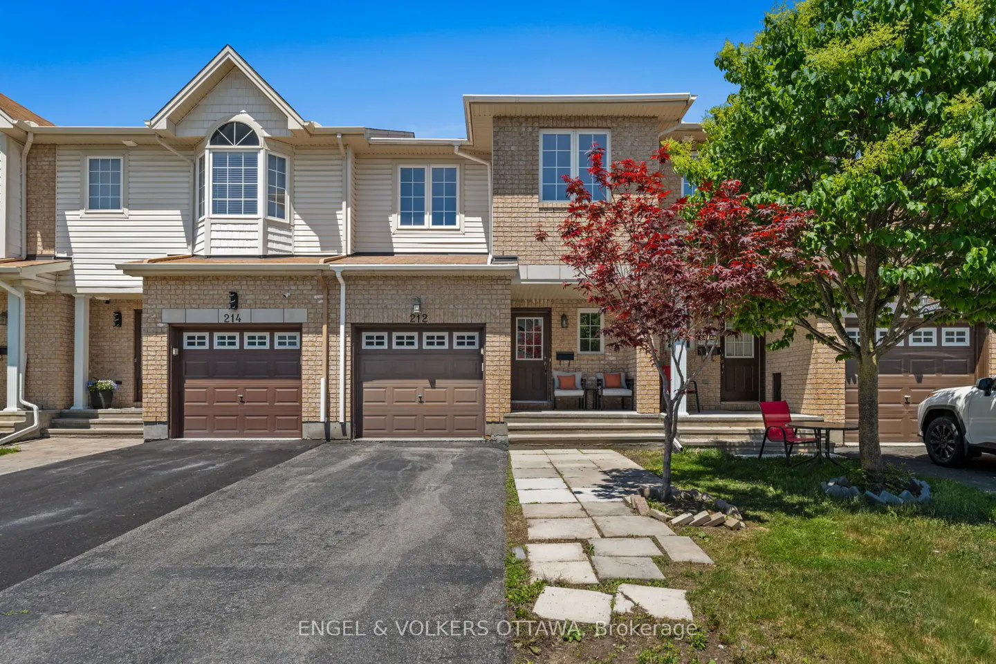 Exterior view of two-story brick and siding townhomes with brown garage doors, a stone walkway, and a red-leafed tree.