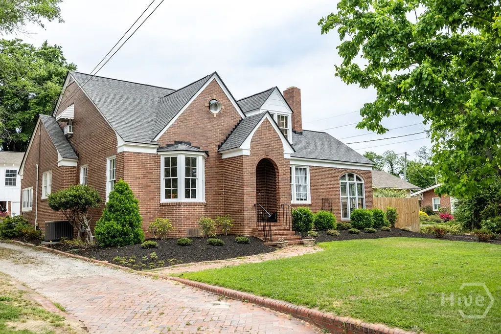 Red brick house with a gray roof, white trim, arched doorway, and manicured lawn.