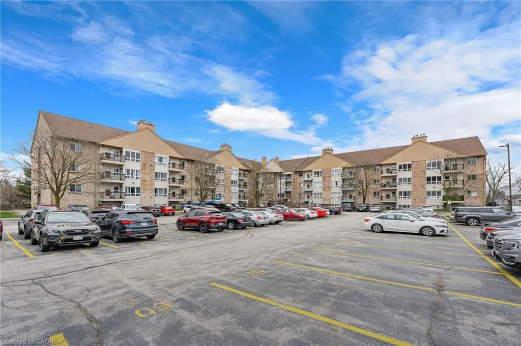 A three-story apartment building with balconies and a full parking lot on a sunny day.