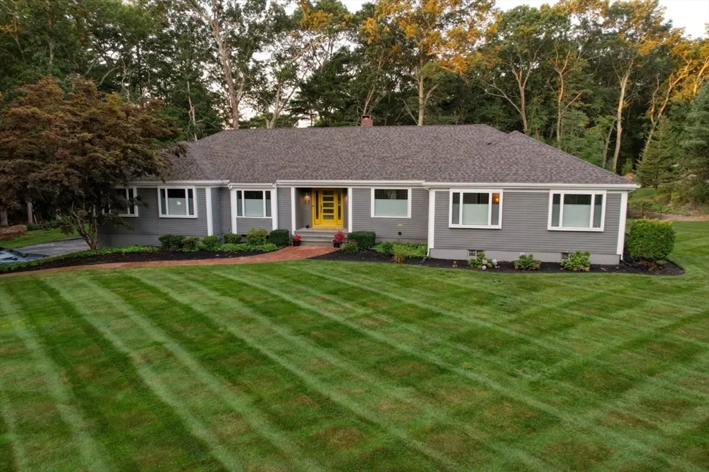 Gray ranch-style house with a yellow front door and manicured lawn with striped pattern. Trees in background.