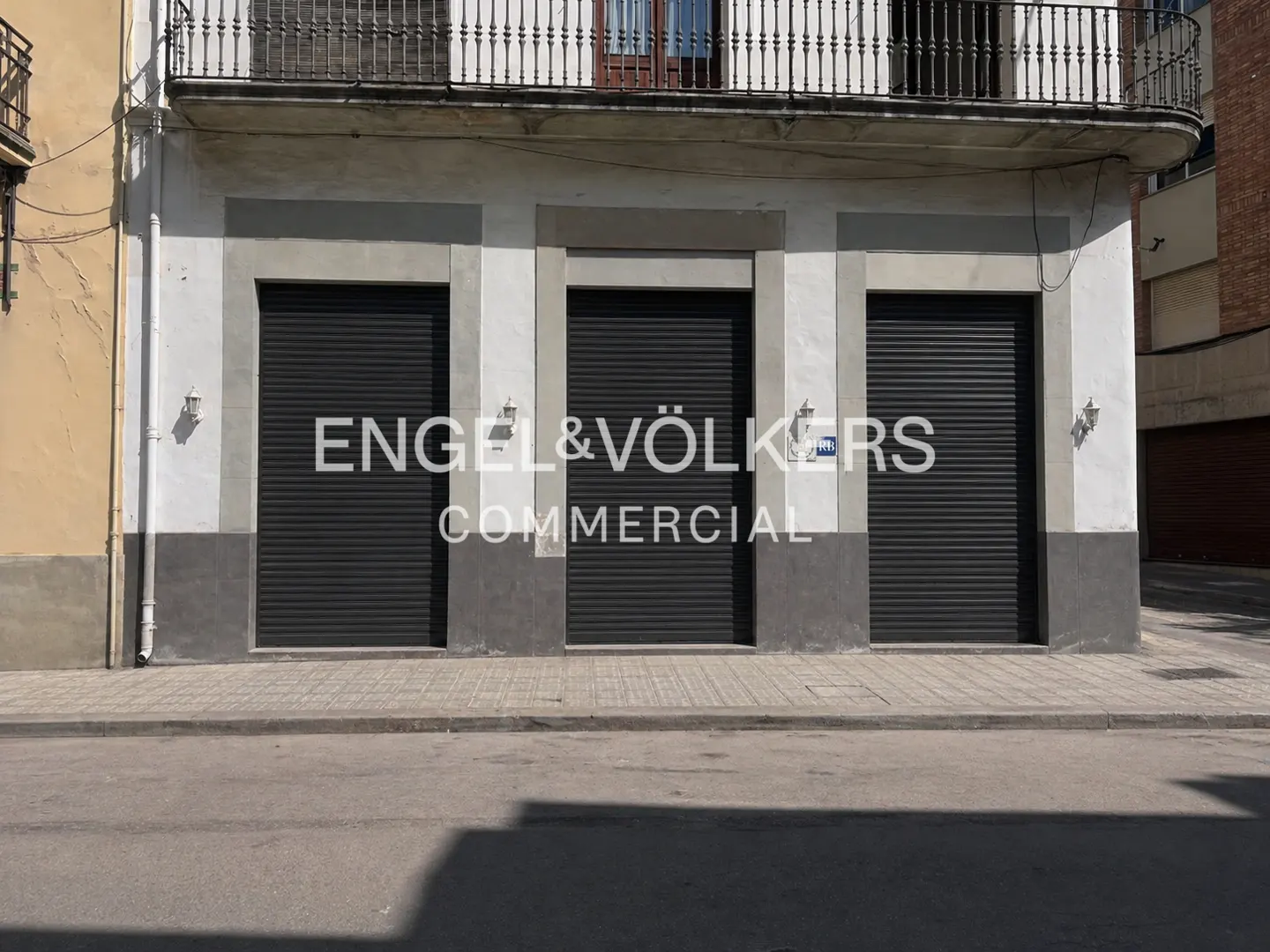 Exterior of Engel & Völkers Commercial building with three closed black shutter doors. Balcony above. Street view.