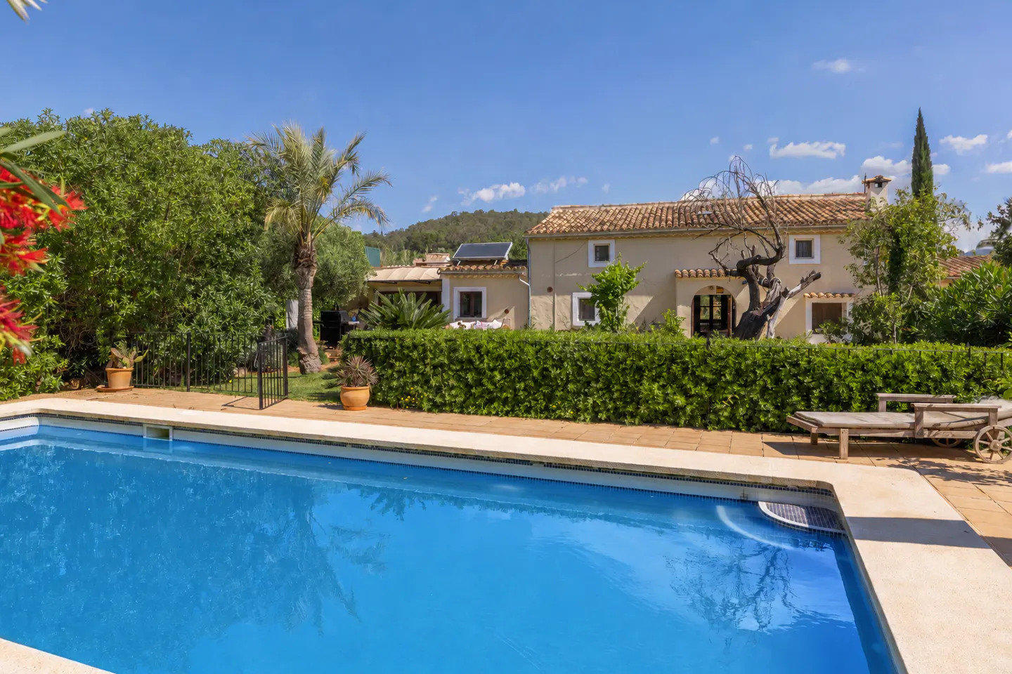A bright blue swimming pool in front of a tan house with a red tile roof.