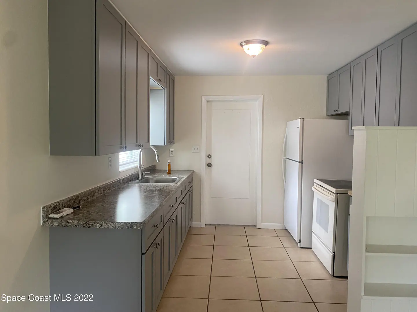 A kitchen with gray cabinets, granite countertops, a white refrigerator, and beige tile flooring.